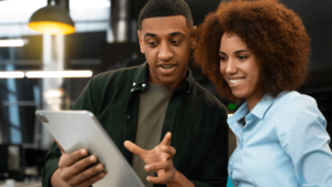 Um homem e uma mulher, ambos negros, sorrindo enquanto analisam informações sobre as fases do processo de mudança em um tablet
