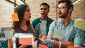 Equipe de homens e mulher discutindo projeto em frente a um quadro de Kanban